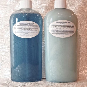 May include: Two clear plastic bottles with blue and green liquid. The bottles are labeled with the text "Ashwagandha Winter Cherry Shampoo & Skin Cleanser" and "Ashwagandha Winter Cherry Conditioner".