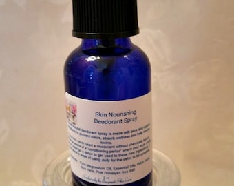 May include: A blue glass bottle of Skin Nourishing Deodorant Spray with a black spray nozzle and a white label. The bottle sits in a clear glass holder. The words "Pampered Skin Care" are written in cursive below the bottle.