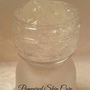 Pode incluir: Um frasco de vidro transparente cheio de uma subst&acirc;ncia espessa, branca e gelatinosa. O frasco tem uma superf&iacute;cie texturizada e o texto "Pampered Skin Care" est&aacute; impresso na parte inferior.
