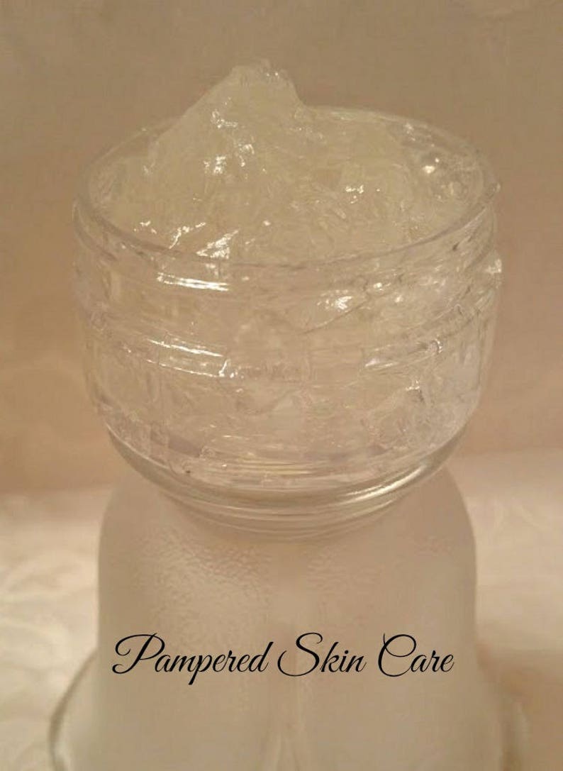 Pode incluir: Um frasco de vidro transparente cheio de uma subst&acirc;ncia espessa, branca e gelatinosa. O frasco tem uma superf&iacute;cie texturizada e o texto "Pampered Skin Care" est&aacute; impresso na parte inferior.