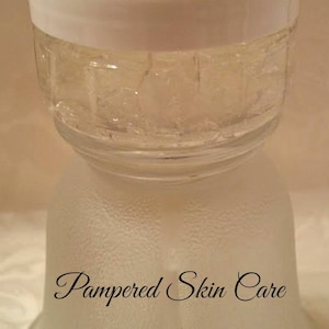 Pode incluir: Um frasco de vidro transparente com uma tampa branca cheio de um gel transparente. O frasco est&aacute; sobre uma superf&iacute;cie branca com as palavras "Pampered Skin Care" escritas nele.