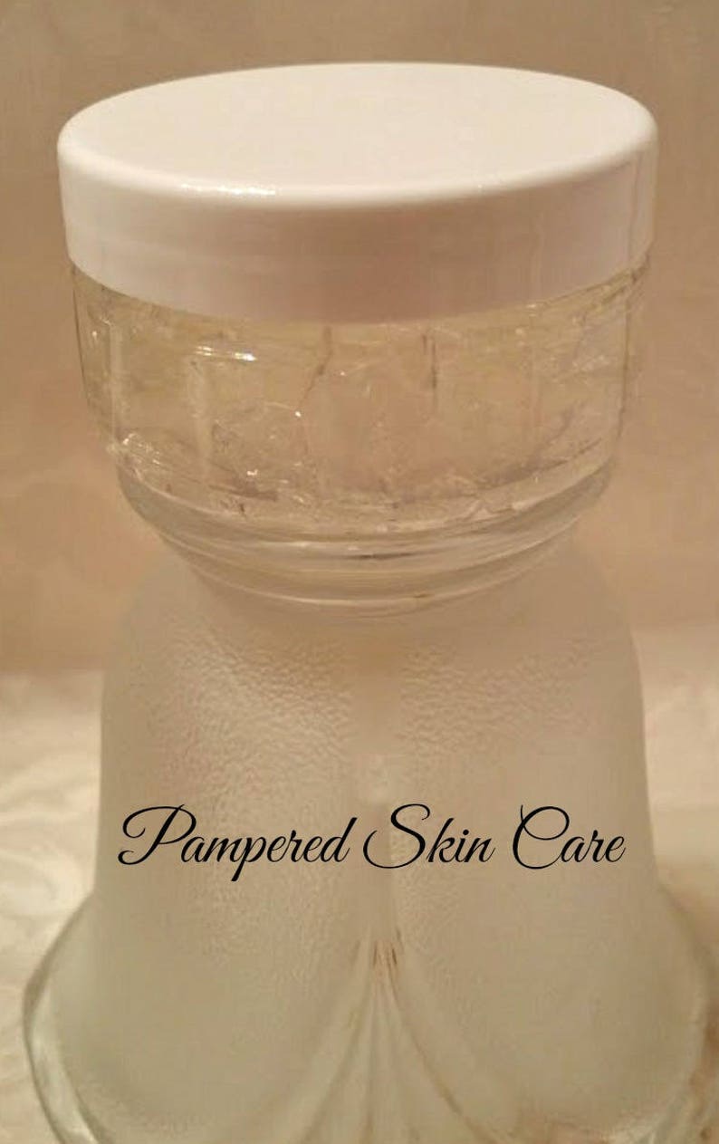 Pode incluir: Um frasco de vidro transparente com uma tampa branca cheio de um gel transparente. O frasco est&aacute; sobre uma superf&iacute;cie branca com as palavras "Pampered Skin Care" escritas nele.