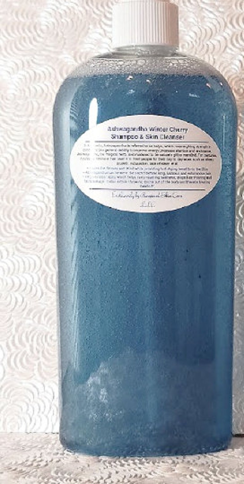 May include: A blue plastic bottle with a white label that reads "Ashwagandha Winter Cherry Shampoo & Skin Cleanser" and "Exclusively by Peaceful Skin Care".