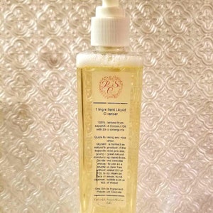 May include: A clear plastic bottle with a white pump dispenser containing a yellow liquid. The bottle has a label with the text "1 Ingredient Liquid Cleanser" and information about the product, including that it is 100% derived from saponified coconut oil with zero detergents.