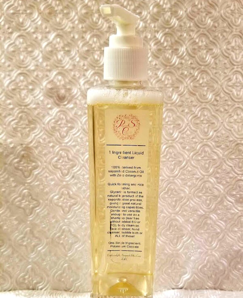 May include: A clear plastic bottle with a white pump dispenser containing a yellow liquid. The bottle has a label with the text "1 Ingredient Liquid Cleanser" and information about the product, including that it is 100% derived from saponified coconut oil with zero detergents.