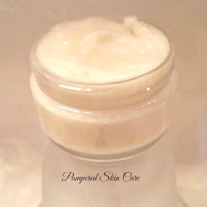 May include: A close-up of a white cream in a glass jar with a white lid. The jar is labeled "Pampered Skin Care".