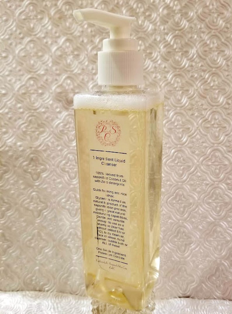 May include: A clear plastic bottle with a white pump dispenser filled with a yellow liquid. The bottle label reads "1 Ingredient Liquid Cleanser" and lists the ingredients as "100% derived from saponified Coconut Oil with Zero detergents".