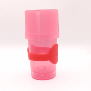 May include: A pink plastic shaker bottle with a matching lid. A red silicone band wraps around the bottle with the word "Save - A" printed on it. The bottle is designed for mixing drinks or supplements.