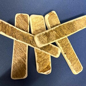 May include: Five rectangular sticks with a smooth, light-colored border and a textured, brown, wood-like center. The sticks are arranged in a crisscross pattern, showcasing a natural, fibrous appearance on the surface of each individual piece.