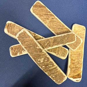 May include: A collection of five rectangular pieces of natural antler material, each featuring a rough, textured brown surface with lighter cream-colored edges. The pieces are arranged in an overlapping, scattered pattern, showcasing the organic, weathered appearance of the bone-like material with distinct ridges and grooves across the surface of each individual segment.