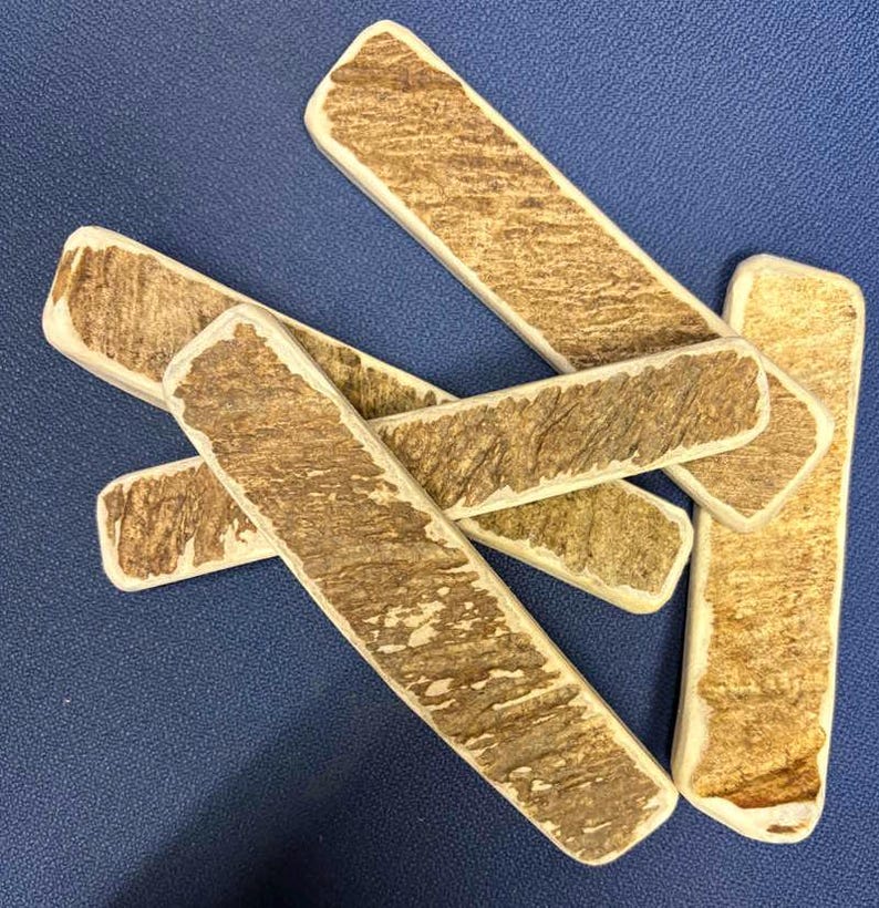 May include: A collection of five rectangular pieces of natural antler material, each featuring a rough, textured brown surface with lighter cream-colored edges. The pieces are arranged in an overlapping, scattered pattern, showcasing the organic, weathered appearance of the bone-like material with distinct ridges and grooves across the surface of each individual segment.