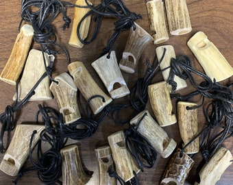 May include: A collection of antler whistles with black cords. The whistles are made from natural antler and have a variety of shapes and sizes.