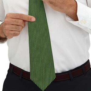 May include: A green striped tie with a white dress shirt and black pants. The tie has vertical stripes in a lighter shade of green. The person is adjusting the tie.