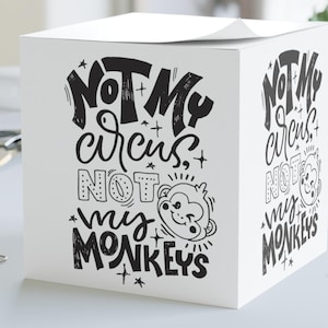 Puede incluir: Bloc de notas blanco en forma de cubo con la frase "NOT MY CIRCUS, NOT MY MONKEYS" en letras negras. También aparece una cara de mono de dibujos animados. El bloc de notas está sobre un escritorio blanco con clips.