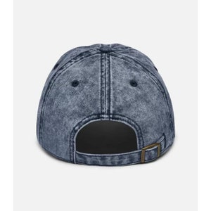 Pode incluir: Um bon&eacute; de beisebol de denim azul escuro com acabamento desbotado. O bon&eacute; tem uma viseira preta e uma correia ajust&aacute;vel marrom.