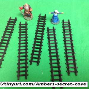 May include: Six black plastic train track pieces, each with 10 rails, on a green surface.