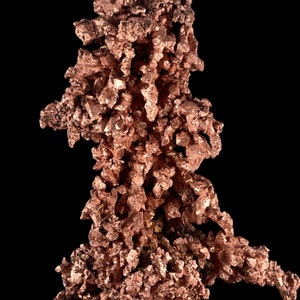 Könnte beinhalten: Ein großer, unregelmäßig geformter Cluster aus Kupferkristallen. Die Kristalle sind tief rotbraun und haben einen metallischen Glanz. Der Cluster wird vor einem schwarzen Hintergrund gezeigt.