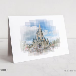 May include: A white greeting card featuring a digitally altered image of a castle with a blue sky background. The image is overlaid with a series of blue squares. The card is leaning against a white surface. The text "MAKE | SHIFT" is at the bottom.
