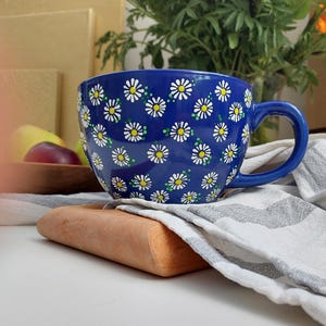 Daisy mug with a white handle, sitting on a wooden coaster