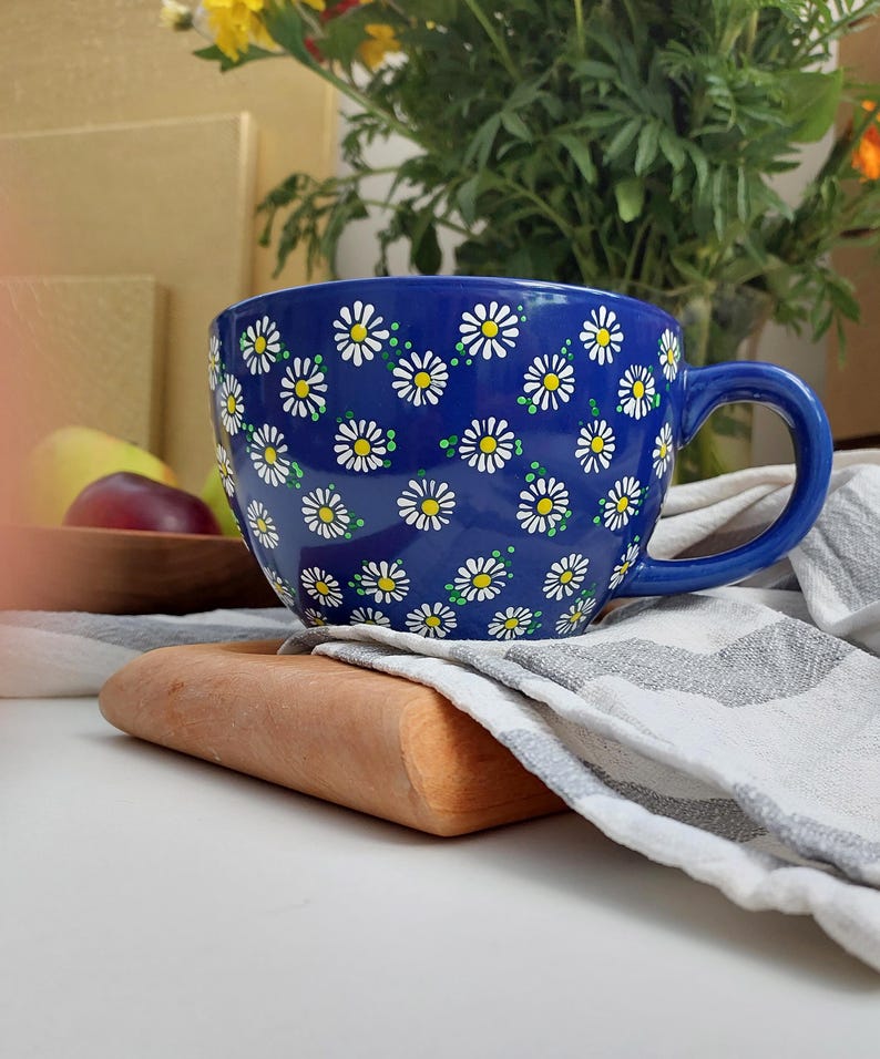 Daisy mug with a white handle, sitting on a wooden coaster