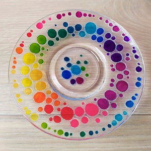 May include: A clear glass plate with a rainbow of colorful dots painted on it. The dots are arranged in a spiral pattern, starting with red and ending with green.