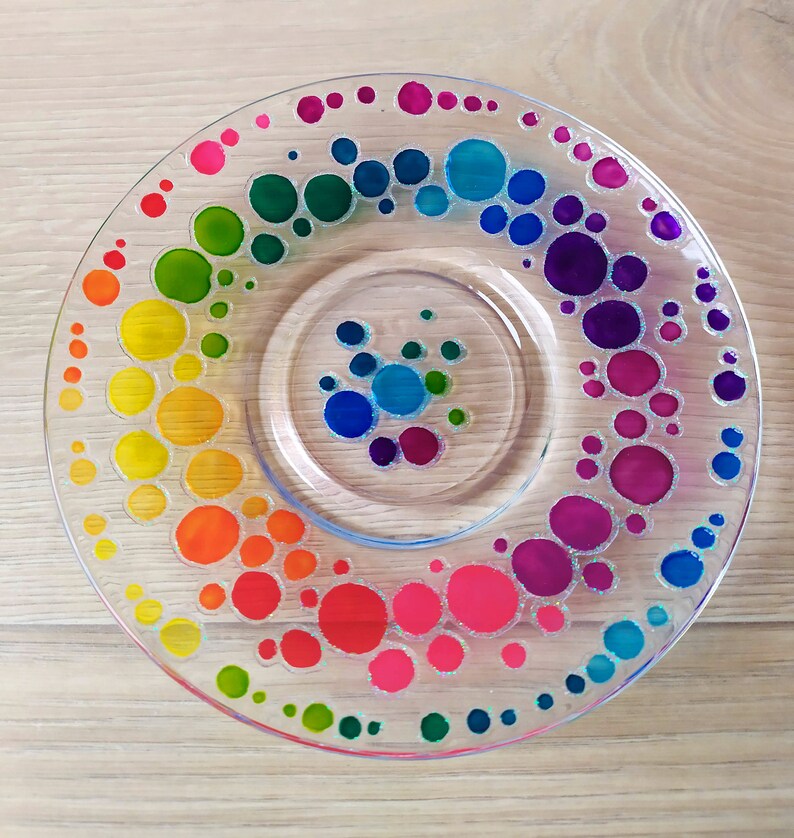 May include: A clear glass plate with a rainbow of colorful dots painted on it. The dots are arranged in a spiral pattern, starting with red and ending with green.