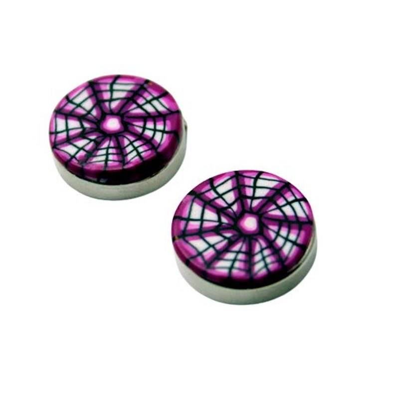Pu&ograve; includere: Due orecchini rotondi con base in metallo color argento. Le parti superiori presentano un design a ragnatela viola e bianca. Gli orecchini sono su uno sfondo bianco.
