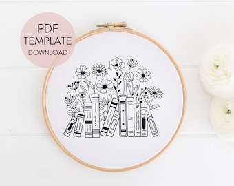 May include: Black and white line art embroidery pattern of a stack of books with flowers growing out of the top. The pattern is in a round embroidery hoop.