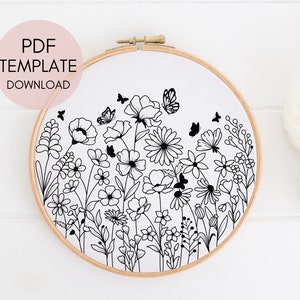 Könnte beinhalten: Schwarz-weißes Linienkunst-Stickmuster eines Blumenstraußes mit Schmetterlingen. Das Muster wird in einem runden Holzstickrahmen angezeigt.