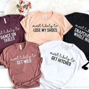 Peut inclure: Cinq t-shirts avec des slogans diff&eacute;rents. Les slogans sont "most likely to dance on tables", "most likely to lose my shoes", "most likely to Snapchat the whole night", "most likely to get wild", et "most likely to get hitched".