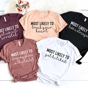 May include: Five t-shirts with different humorous sayings printed on them. The sayings are "Most Likely To Get Us All Arrested", "Most Likely To Break Your Heart", "Most Likely To Drop My Phone In The Toilet", "Most Likely To Kiss A Stranger", and "Most Likely To Get Hitched".
