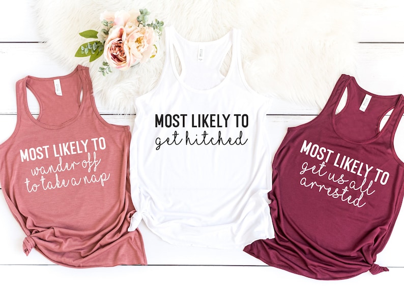 May include: Three tank tops with white text on different colored backgrounds. The text on the pink tank top reads "MOST LIKELY TO wander off to take a nap". The text on the white tank top reads "MOST LIKELY TO get hitched". The text on the maroon tank top reads "MOST LIKELY TO get us all arrested".