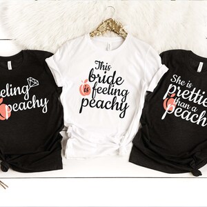 May include: Three black and white t-shirts with peach and diamond graphics. The shirts say "feeling peachy", "This bride is feeling peachy", and "She is prettier than a peach".