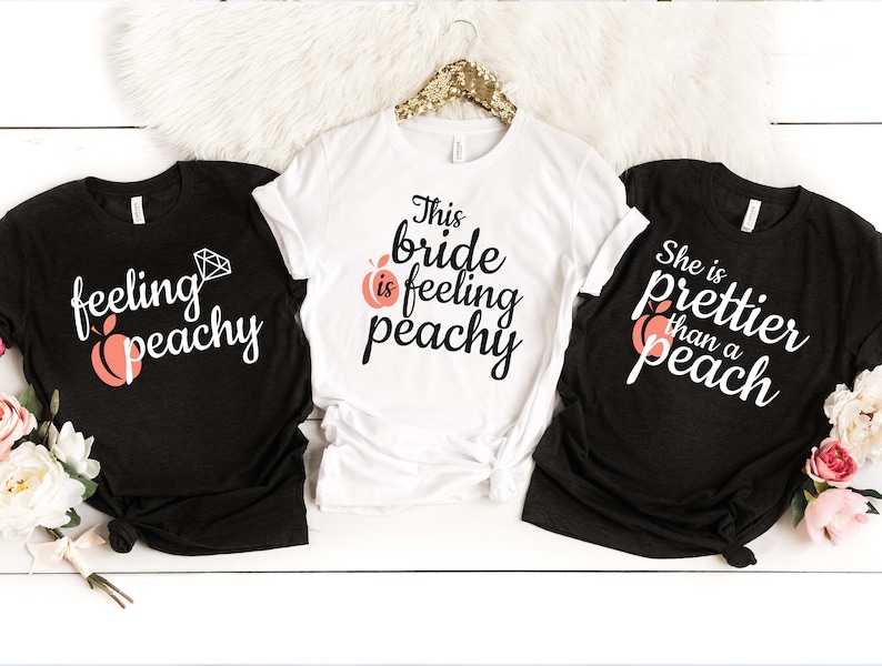 May include: Three black and white t-shirts with peach and diamond graphics. The shirts say "feeling peachy", "This bride is feeling peachy", and "She is prettier than a peach".