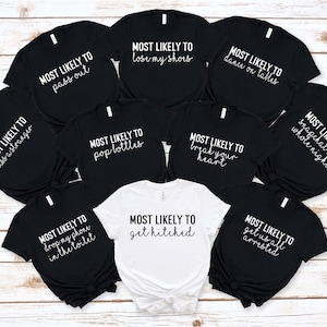 May include: Nine black t-shirts with white text that says "Most Likely To" followed by a different phrase on each shirt. One white t-shirt with black text that says "Most Likely To get hitched".