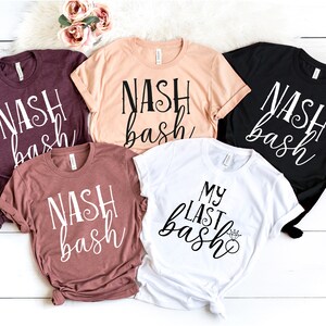 May include: Five t-shirts in shades of burgundy, peach, rose, black, and white. Each shirt displays the text "NASH bash" in a cursive font, except for the white shirt, which reads "MY LAST bash" with a diamond ring graphic.
