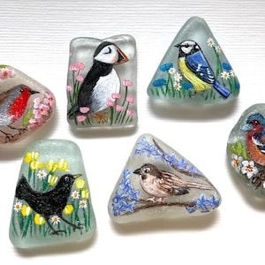 May include: Six painted glass stones, each featuring a different bird species. The birds are painted in realistic detail and surrounded by flowers. The stones are a unique and charming way to add a touch of nature to your home.
