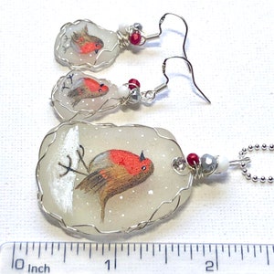 May include: A set of three robin bird ornaments, each with a different pose, painted on a white glass background. The ornaments are wrapped in silver wire and have red and silver beads. The largest ornament is about 2 inches long.