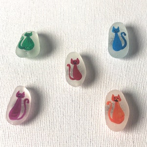 May include: Five glass cat figurines with painted details. Each figurine is a different colour: green, red, blue, purple, and orange.