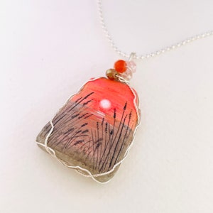 Könnte beinhalten: Eine silberne Kettenkette mit einem Anhänger, der eine handgemalte Sonnenuntergangsszene auf einem Stein zeigt. Der Stein ist mit Silberdraht umwickelt und die Kette hat orangefarbene und klare Perlen.