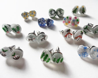 May include: A set of 10 pairs of Christmas-themed earrings. Each pair features a different design, including snowflakes, reindeer, Christmas trees, holly, and snowmen. The earrings are made of glass and have silver posts.
