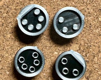 May include: Four round black and silver game pieces with different numbers of white dots on each piece. The pieces are made of plastic and have a textured surface.
