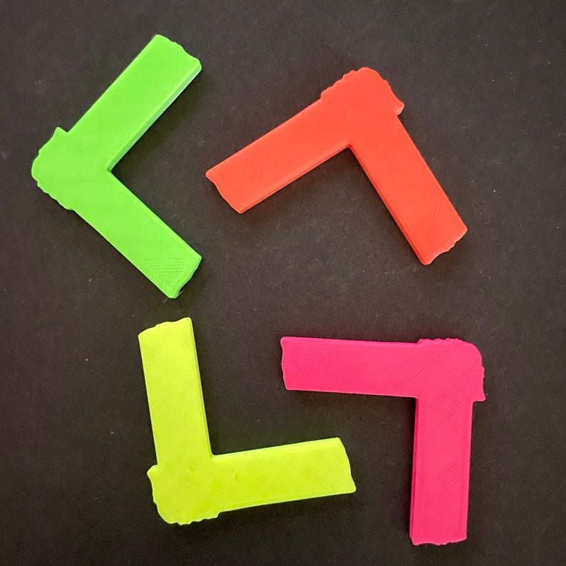 May include: Four plastic corner pieces in different colors: green, red, yellow, and pink. The corner pieces are all the same size and shape.