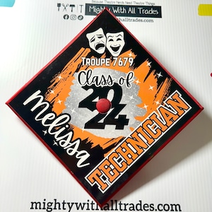 May include: A black and orange graduation cap with a red border. The cap has a silver glitter background with the text "Class of 22" and "Troupe 7679". The name "Melissa" is written in white cursive and "Technician" is written in orange. Two white masks are at the top of the cap.