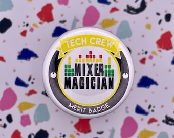Könnte beinhalten: Ein weißer Knopf mit einem schwarzen und gelben Design. Der Knopf trägt die Aufschrift "Tech Crew Mixer Magician Merit Badge".
