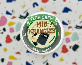 Könnte beinhalten: Ein weißer Knopf mit grünem und schwarzem Design. Der Knopf trägt die Aufschrift "Tech Crew Mic Wrangler Merit Badge" mit einem Mikrofon und einem Funkgerät.