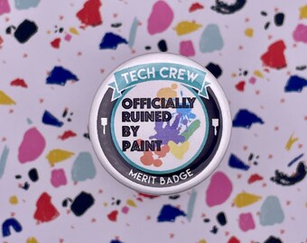 Puede incluir: Un botón blanco con un borde negro y el texto "Tech Crew Officially Ruined By Paint Merit Badge" en una fuente colorida.