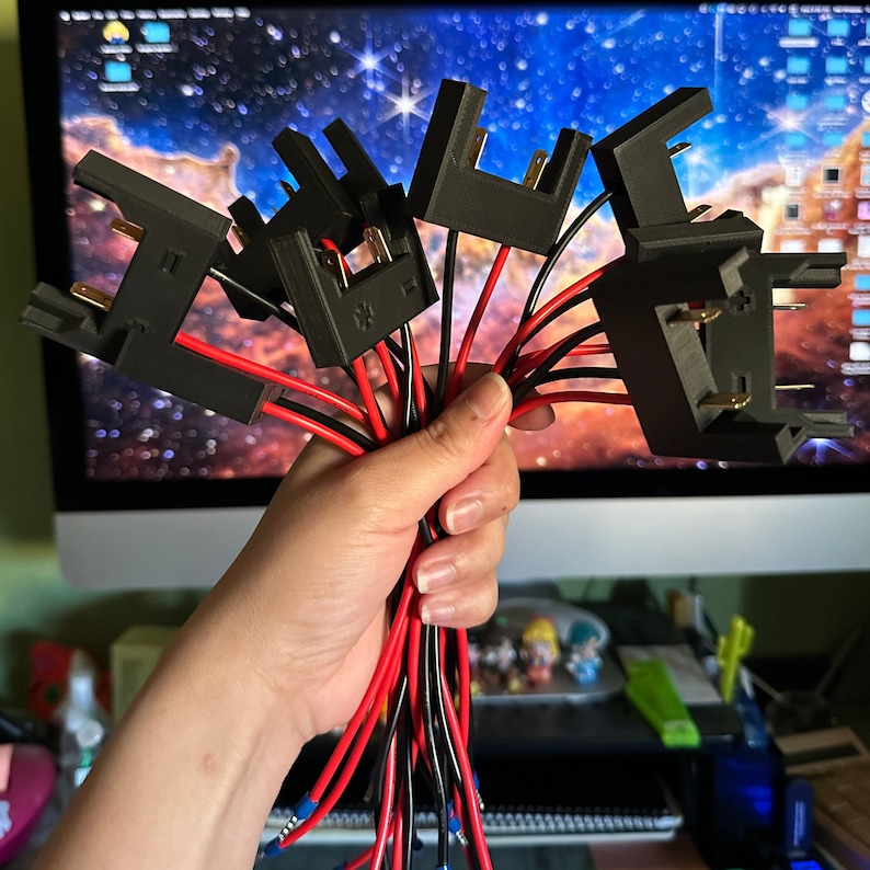 May include: A close-up of a hand holding a bundle of black electrical connectors with red and black wires. The connectors have small metal prongs and are likely used for electrical wiring.
