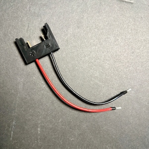 May include: A black plastic connector with two wires, one red and one black, attached. The wires are connected to the connector with small metal terminals.