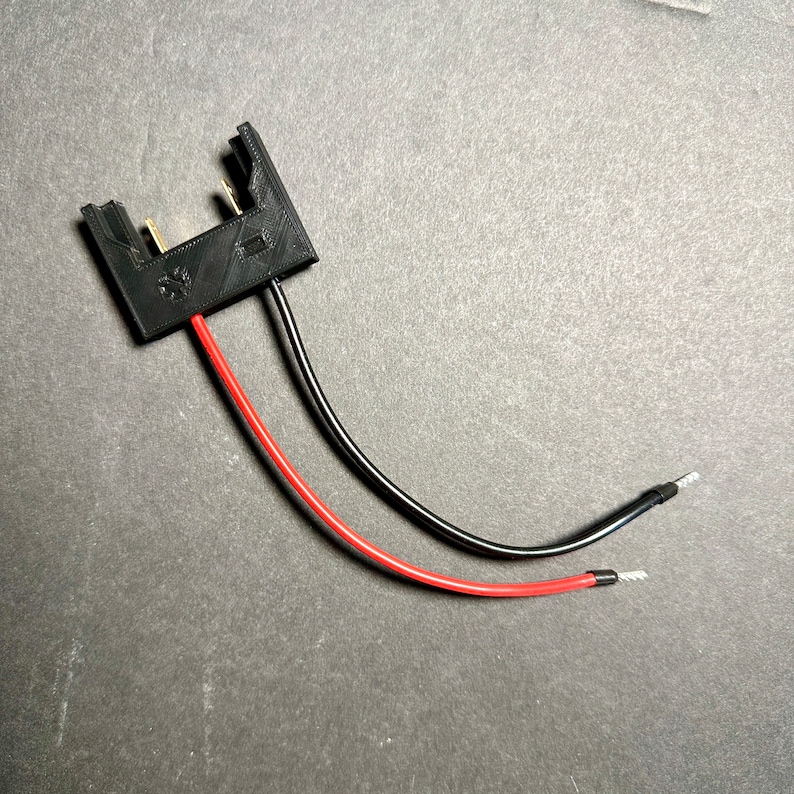 May include: A black plastic connector with two wires, one red and one black, attached. The wires are connected to the connector with small metal terminals.